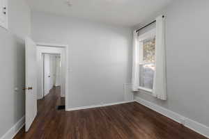 Spare room featuring dark wood-style floors and baseboards