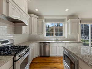 Kitchen with appliances with stainless steel finishes, premium range hood, dark wood-style flooring, light stone counters, and recessed lighting