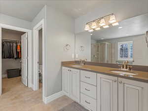Bathroom with a walk in closet, a stall shower, double vanity, and light tile patterned floors