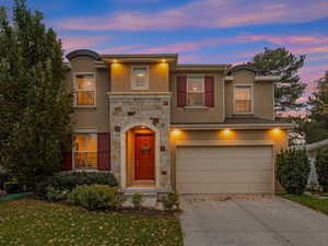 View of front of house featuring stone siding, stucco siding, concrete driveway, an attached garage, and a lawn
