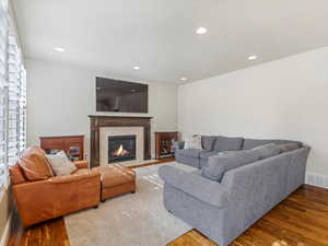 Living room with a fireplace with flush hearth, wood finished floors, and recessed lighting