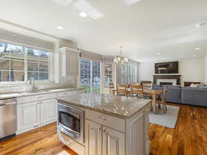 Kitchen with light stone counters, light wood-style flooring, stainless steel appliances, decorative light fixtures, and a fireplace