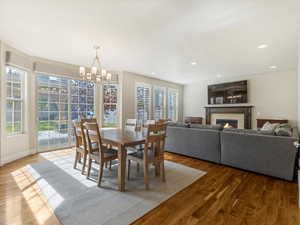Dining area featuring a warm lit fireplace, wood finished floors, a chandelier, and recessed lighting