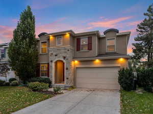 View of front of house with stucco siding, stone siding, a front yard, concrete driveway, and an attached garage