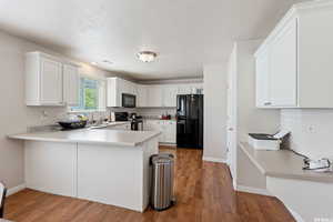 Kitchen with white cabinetry, light countertops, black appliances, a peninsula, and light wood-type flooring