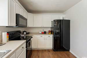 Kitchen with black appliances, dark wood-style flooring, light countertops, and white cabinets