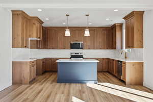 Kitchen featuring a kitchen island, hanging light fixtures, brown cabinetry, decorative backsplash, and recessed lighting