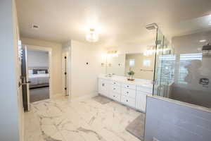 Ensuite bathroom with double vanity, light marble finish floors, a textured ceiling, and a shower stall