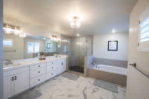 Bathroom featuring healthy amount of natural light, double vanity, a bath, a textured ceiling, and a stall shower
