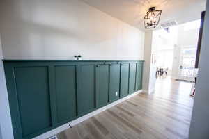 Hall with light wood-type flooring, a chandelier, and a decorative wall