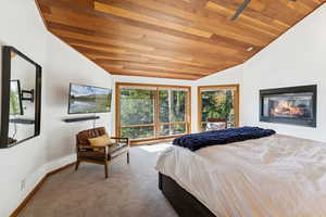 Carpeted bedroom with wood ceiling, lofted ceiling, and a glass covered fireplace