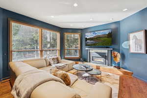 Living area with wood finished floors, a tiled fireplace, and recessed lighting
