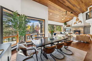 Dining space with dark wood finished floors, high vaulted ceiling, wood ceiling, and a stone fireplace