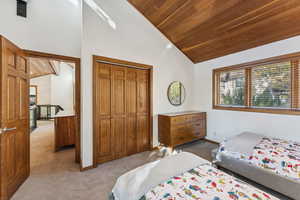 Bedroom with light carpet, wooden ceiling, a closet, and high vaulted ceiling
