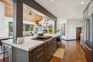 Kitchen featuring stainless steel appliances, a breakfast bar area, dark wood-style flooring, a center island with sink, and a fireplace