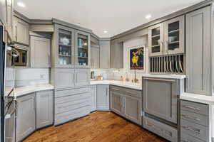 Kitchen featuring gray cabinetry, glass insert cabinets, dark wood-style flooring, recessed lighting, and light stone counters
