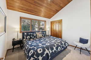 Bedroom featuring wood ceiling, light colored carpet, a closet, and high vaulted ceiling