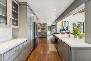 Kitchen featuring gray cabinets, dark wood finished floors, glass insert cabinets, recessed lighting, and light stone counters