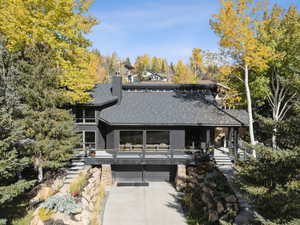 Back of property with a chimney, driveway, view of scattered trees, a shingled roof, and a deck