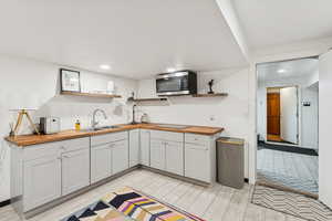 Kitchen with open shelves, wood counters, light wood-style floors, stainless steel microwave, and recessed lighting