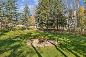 View of green lawn featuring a patio area and a fire pit