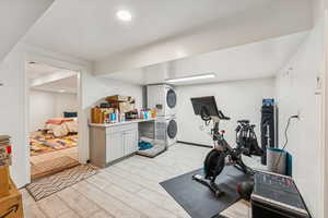 Exercise room with stacked washing machine and dryer, light wood-type flooring, and recessed lighting
