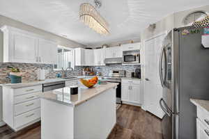 Kitchen with stainless steel appliances, white cabinetry, a kitchen island, light stone counters, and tasteful backsplash