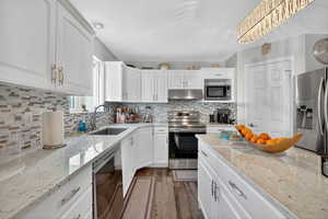 Kitchen with white cabinetry, appliances with stainless steel finishes, and light stone counters