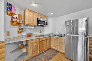Kitchen with stainless steel appliances, open shelves, a textured ceiling, light brown cabinets, and light wood-style floors