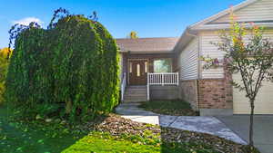Entrance to property featuring brick siding, a porch, and roof with shingles