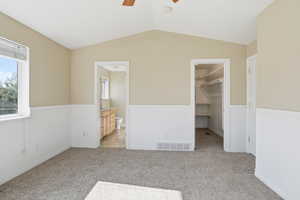 Unfurnished bedroom featuring a spacious closet, light colored carpet, multiple windows, vaulted ceiling, and a ceiling fan