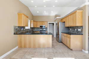 Kitchen with light brown cabinets, backsplash, a peninsula, dark stone counters, and lofted ceiling
