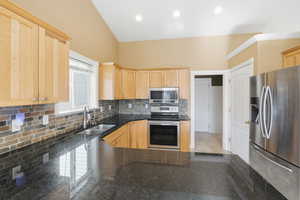 Kitchen featuring appliances with stainless steel finishes, light brown cabinetry, tasteful backsplash, dark stone counters, and recessed lighting
