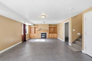 Unfurnished living room with a tiled fireplace, stairs, and built in features