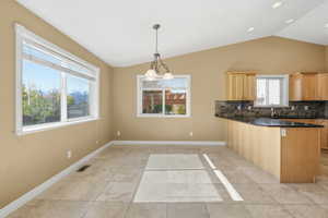 Kitchen with decorative backsplash, lofted ceiling, hanging light fixtures, a peninsula, and light tile patterned flooring