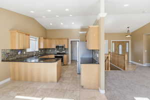 Kitchen with tasteful backsplash, light brown cabinets, dark stone countertops, a peninsula, and vaulted ceiling