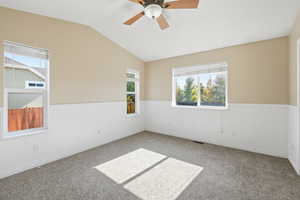 Carpeted empty room with lofted ceiling, a wainscoted wall, and a ceiling fan