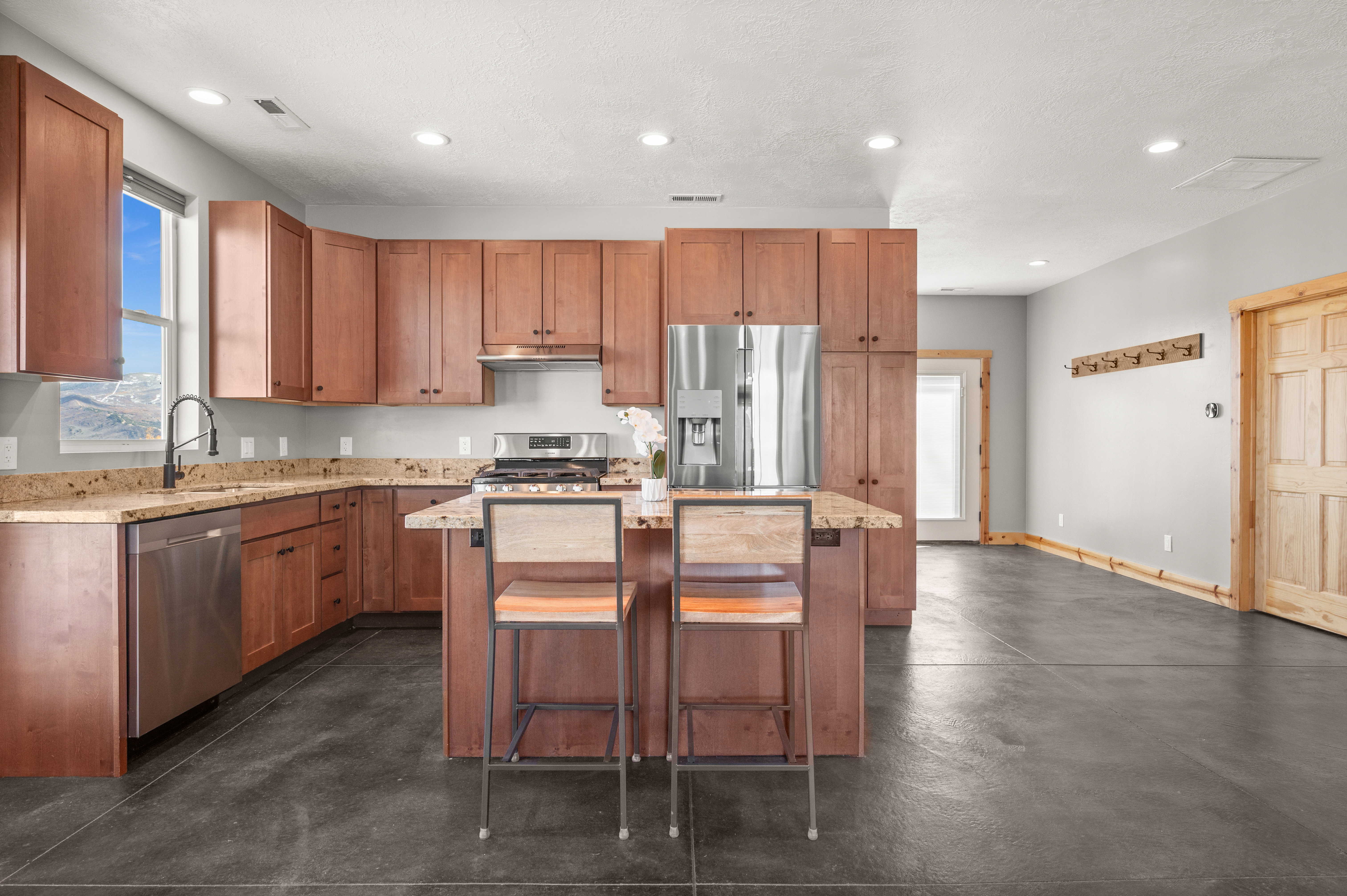 Kitchen featuring light stone counters, appliances with stainless steel finishes, brown cabinetry, a kitchen island, and recessed lighting