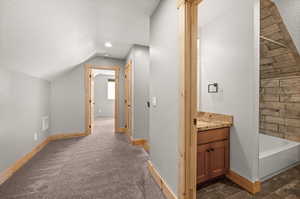 Hallway with a textured ceiling, lofted ceiling, and dark carpet