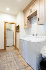 Laundry room featuring light wood-style flooring, washing machine and dryer, recessed lighting, and cabinet space