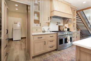 Kitchen with custom exhaust hood, light brown cabinets, double oven range, recessed lighting, and freestanding refrigerator