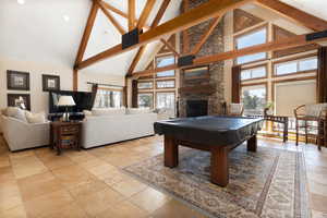 Rec room with high vaulted ceiling, pool table, a fireplace, beamed ceiling, and stone tile flooring