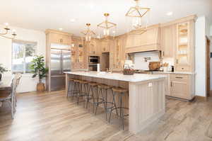 Kitchen featuring glass insert cabinets, a chandelier, light brown cabinets, a kitchen breakfast bar, and stainless steel appliances
