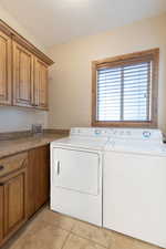 Laundry area with cabinet space, washing machine and dryer, a textured ceiling, and stone tile floors