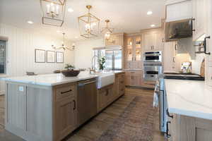 Kitchen with light stone counters, appliances with stainless steel finishes, glass insert cabinets, light brown cabinets, and recessed lighting