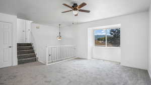 Unfurnished room with light colored carpet, ceiling fan, and stairs