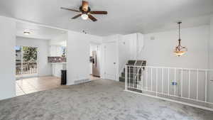 Spare room featuring light carpet, light tile patterned flooring, ceiling fan, and stairs