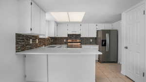 Kitchen featuring appliances with stainless steel finishes, white cabinets, light stone countertops, light tile patterned flooring, and backsplash