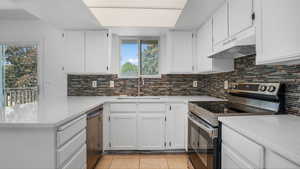 Kitchen featuring stainless steel appliances, decorative backsplash, light stone countertops, and white cabinets