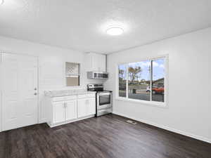 Kitchen featuring appliances with stainless steel finishes, white cabinets, a textured ceiling, subway-style backsplash, and dark LVP floors